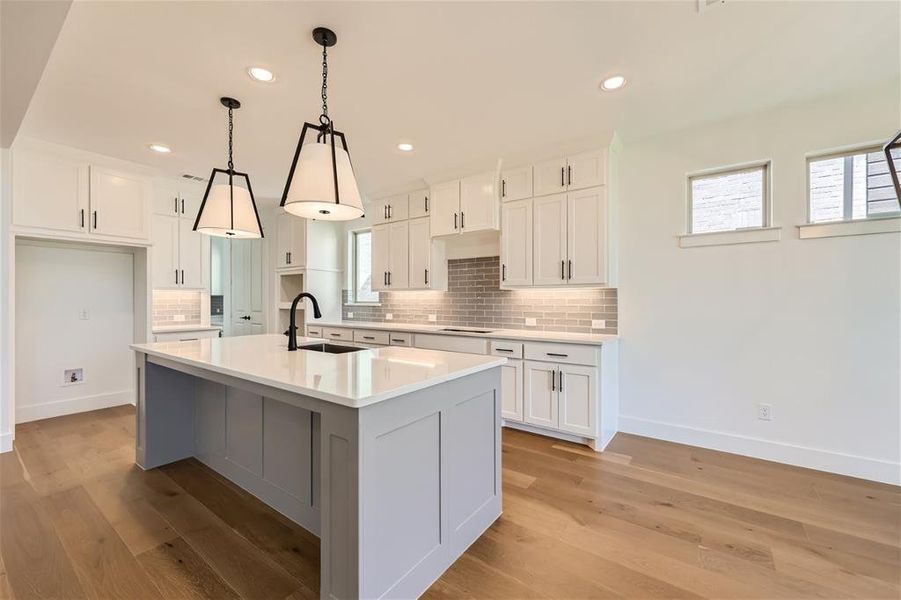 Kitchen featuring sink, light hardwood / wood-style flooring, white cabinets, and a kitchen island with sink