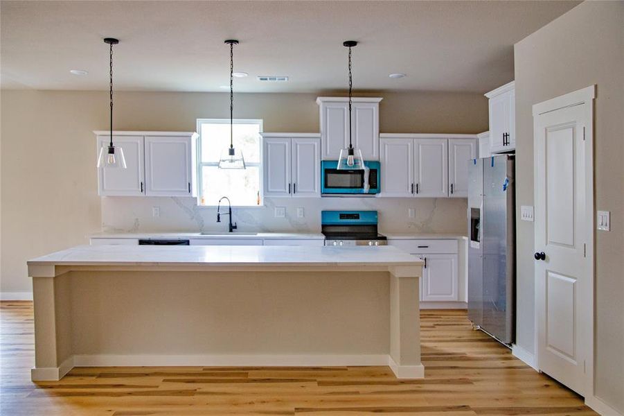 Kitchen with white cabinetry, appliances with stainless steel finishes, hanging light fixtures, a kitchen island, and light wood-type flooring