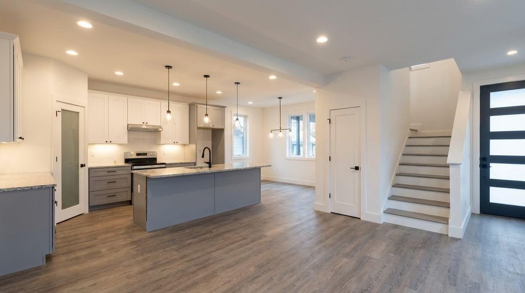 Kitchen with gray cabinets, an island with sink, white cabinets, pendant lighting, and dark wood finished floors