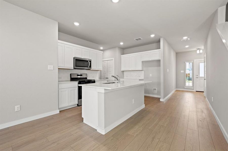 Kitchen with a kitchen island with sink, white cabinets, and appliances with stainless steel finishes