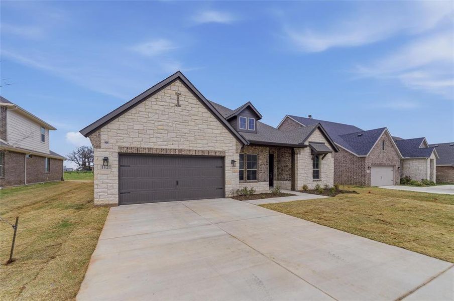 View of front of home featuring a front lawn, a garage, stone siding, and driveway