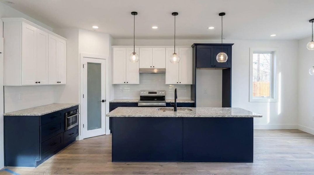 Kitchen with dual tone cabinetry, light wood-style flooring, hanging light fixtures, electric stove, and light stone counters