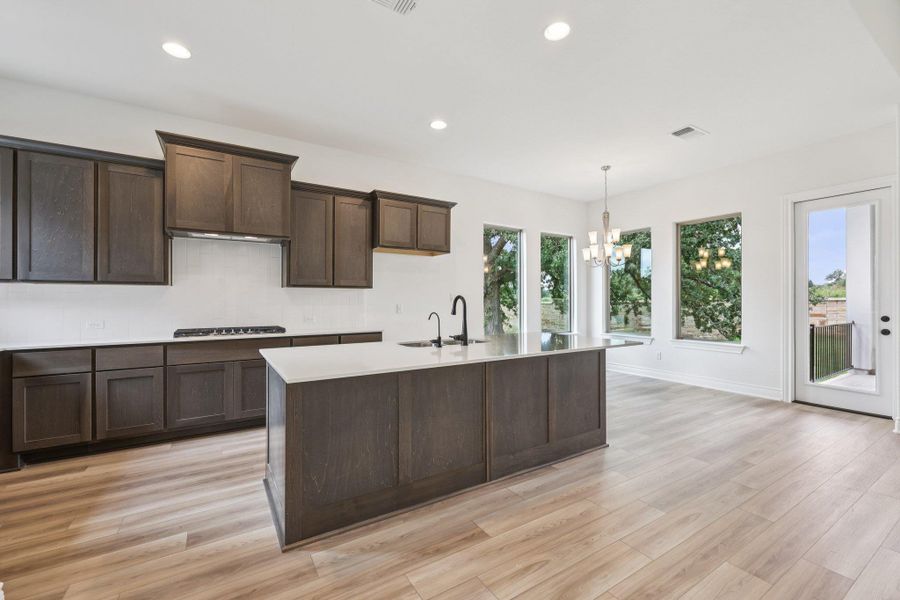 Kitchen featuring recessed lighting, dark brown cabinetry, light wood finished floors, hanging light fixtures, and light stone counters