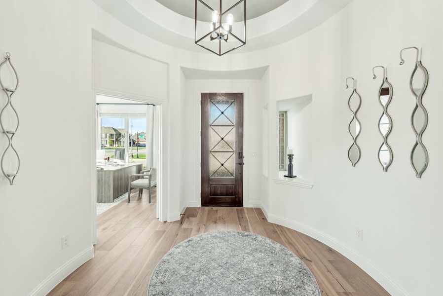 Foyer with round tray ceiling, dark wood front door with glass panels, chandelier, and light hardwood floors Foyer with round tray ceiling, dark wood front door with glass panels, chandelier, and light hardwood floors