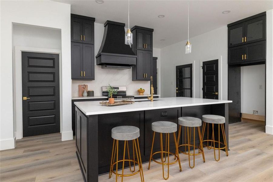 Kitchen with a center island with sink, pendant lighting, range, and premium range hood