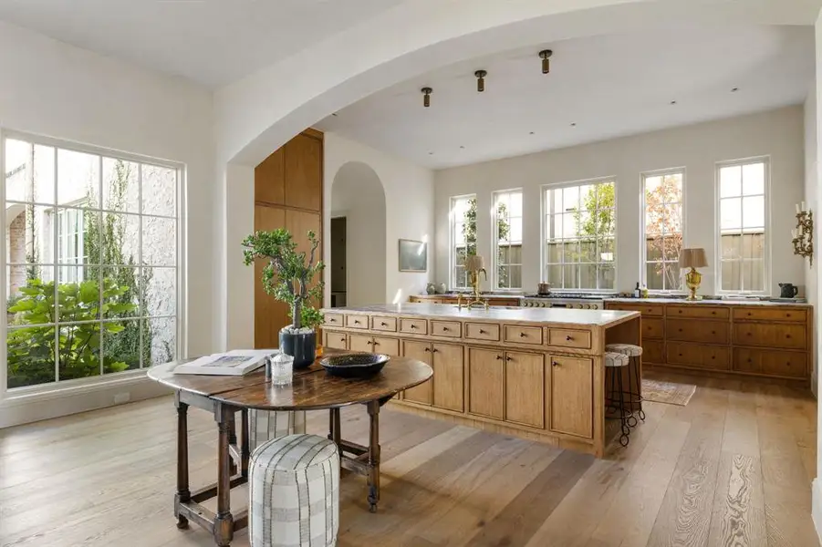 Kitchen with light wood finished floors, light countertops, arched walkways, and a center island with sink