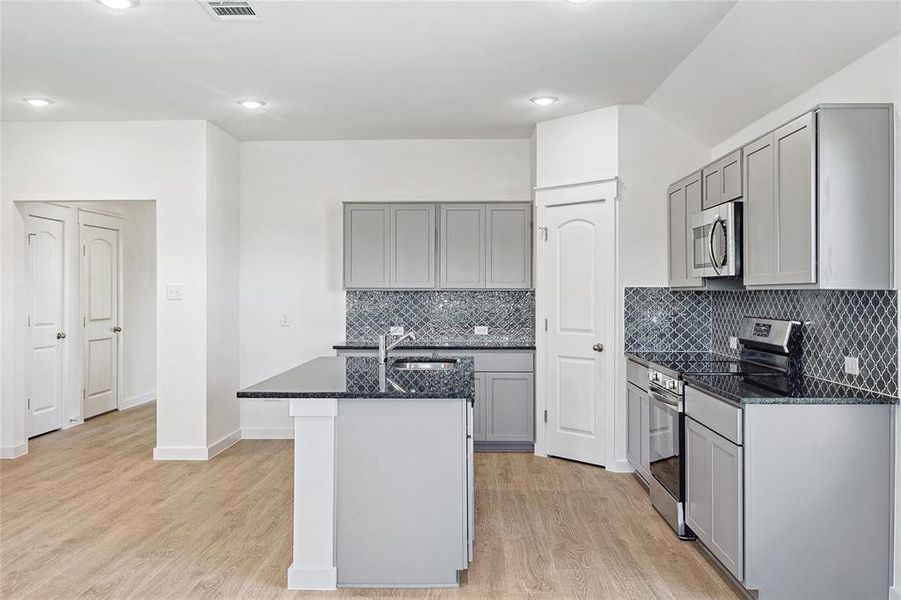 Kitchen featuring a kitchen island with sink, stainless steel appliances, gray cabinetry, and light hardwood / wood-style floors