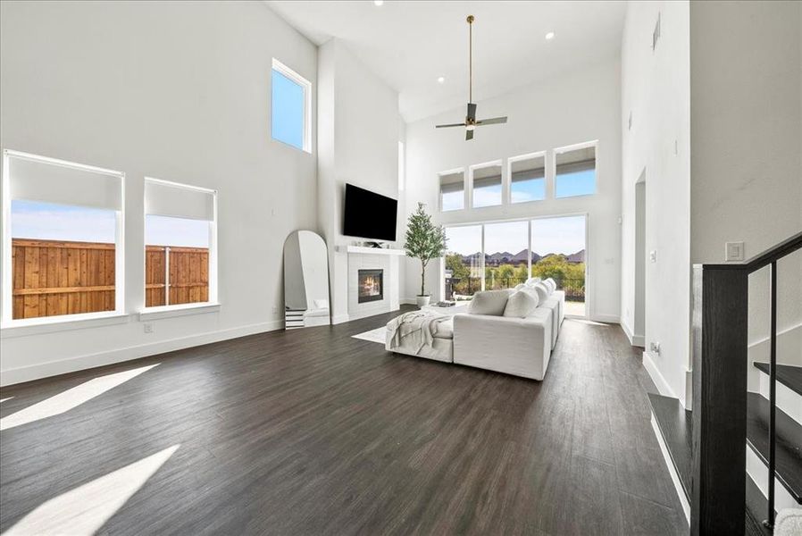 Living area with dark wood-style floors, a glass covered fireplace, stairway, and baseboards