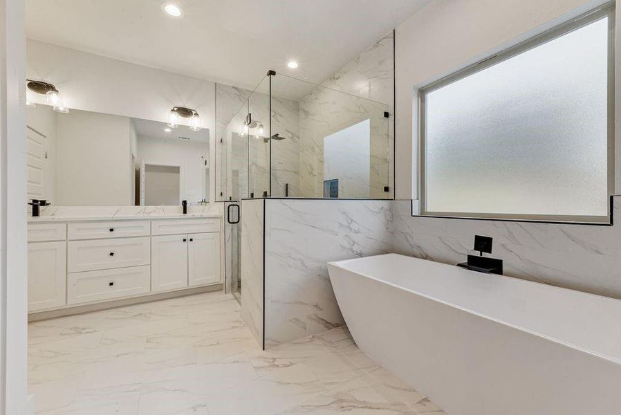 Bathroom featuring a freestanding tub, double vanity, a marble finish shower, light marble finish flooring, and recessed lighting Bathroom featuring a freestanding tub, double vanity, a marble finish shower, light marble finish flooring, and recessed lighting