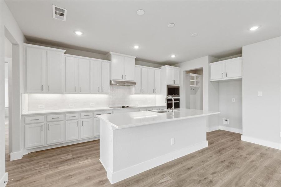 Kitchen featuring stainless steel microwave, black electric cooktop, under cabinet range hood, a kitchen island with sink, and white cabinetry Kitchen featuring stainless steel microwave, black electric cooktop, under cabinet range hood, a kitchen island with sink, and white cabinetry