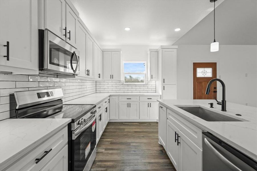 Kitchen featuring sink, decorative light fixtures, white cabinets, and appliances with stainless steel finishes