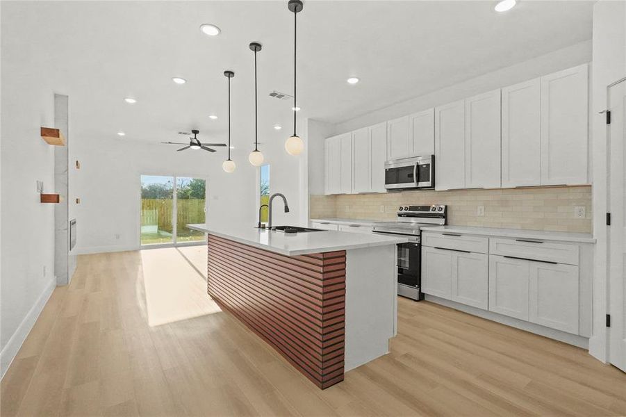 Kitchen with white cabinets, stainless steel appliances, a center island with sink, a ceiling fan, and light wood-style floors
