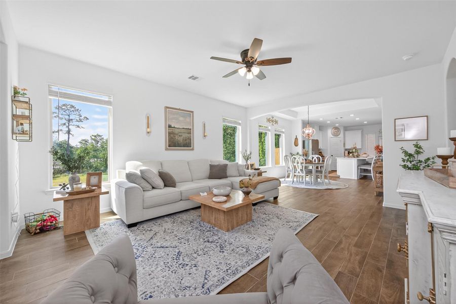 This is a bright, open-concept living area featuring a cozy seating arrangement, wood tile flooring, and large windows offering natural light and scenic views. It seamlessly connects to a dining area and kitchen, creating a spacious and inviting atmosphere perfect for entertaining. This is a bright, open-concept living area featuring a cozy seating arrangement, wood tile flooring, and large windows offering natural light and scenic views. It seamlessly connects to a dining area and kitchen, creating a spacious and inviting atmosphere perfect for entertaining.