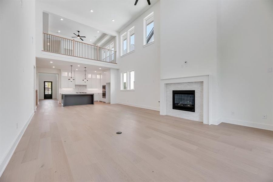 Unfurnished living room with light wood finished floors, a glass covered fireplace, recessed lighting, ceiling fan, and a high ceiling