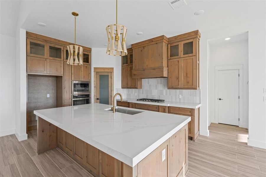 Kitchen with a center island with sink, sink, light wood-type flooring, appliances with stainless steel finishes, and decorative light fixtures