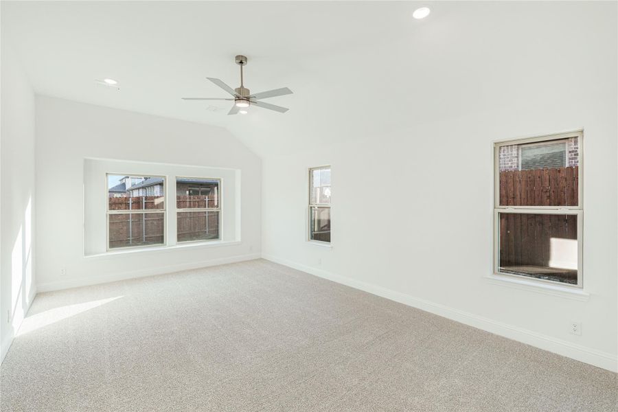 Empty room with vaulted ceiling, ceiling fan, carpet flooring, and multiple windows with backyard views