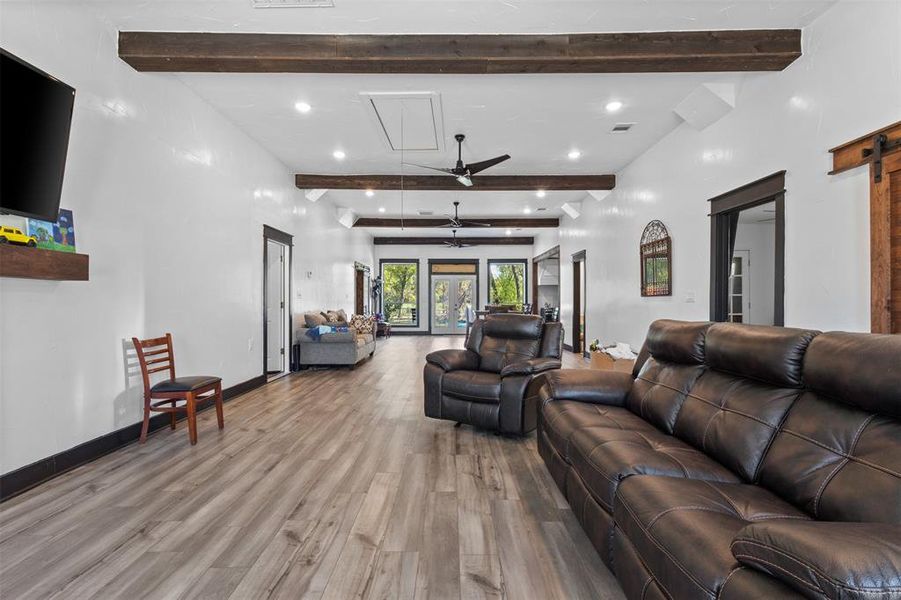 Living room featuring wood finished floors, beamed ceiling, ceiling fan, recessed lighting, and a barn door Living room featuring wood finished floors, beamed ceiling, ceiling fan, recessed lighting, and a barn door