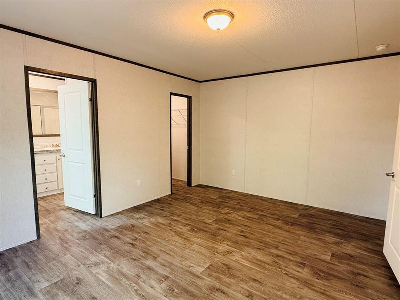 Unfurnished bedroom featuring wood finished floors, a textured ceiling, ornamental molding, and a closet