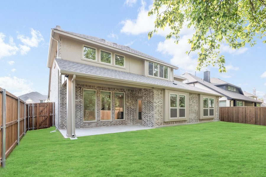 Two-story brick home with covered back patio, large windows, and fenced green backyard