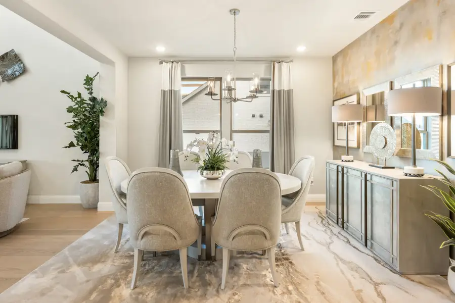 Formal dining room with round white table, six upholstered chairs, chandelier, and sideboard on patterned area rug