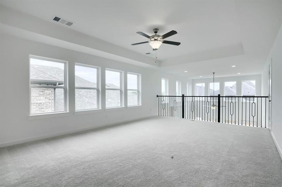 Spacious room featuring light gray carpeting, multiple windows, a ceiling fan, and a balcony with black metal balusters