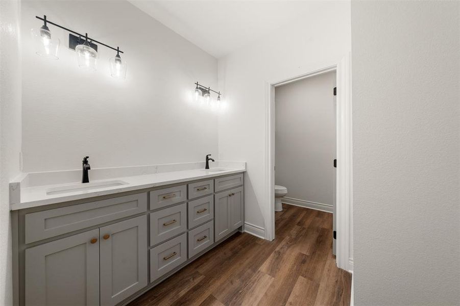 Bathroom featuring double vanity and dark wood-style flooring Bathroom featuring double vanity and dark wood-style flooring