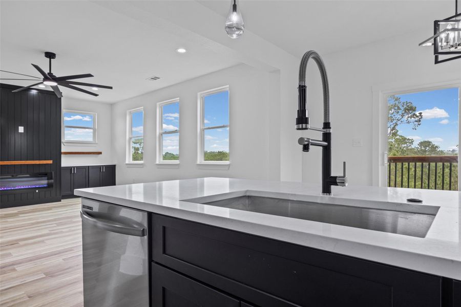 Kitchen island featuring a stainless steel sink with a modern gooseneck faucet, integrated dishwasher, and a light-toned countertop Kitchen island featuring a stainless steel sink with a modern gooseneck faucet, integrated dishwasher, and a light-toned countertop