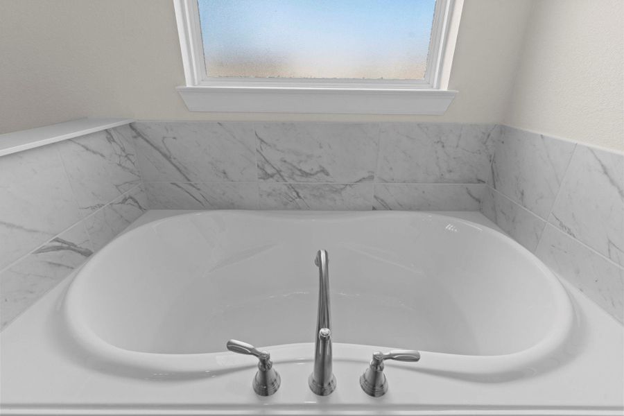 Luxurious soaking tub surrounded by marble-style tile, ideal for relaxation after a long day.