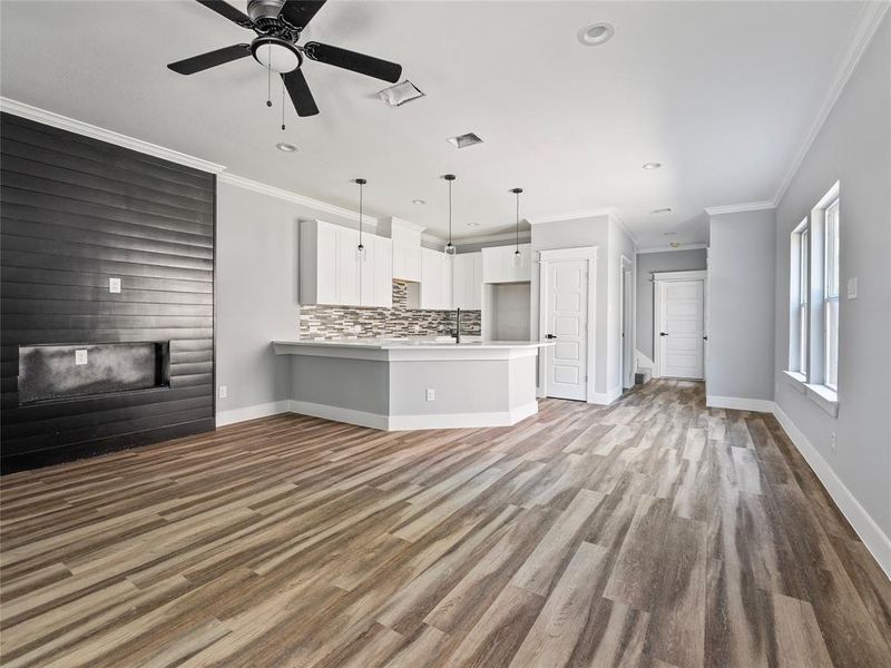 Unfurnished living room with a glass covered fireplace, a sink, crown molding, baseboards, and wood finished floors