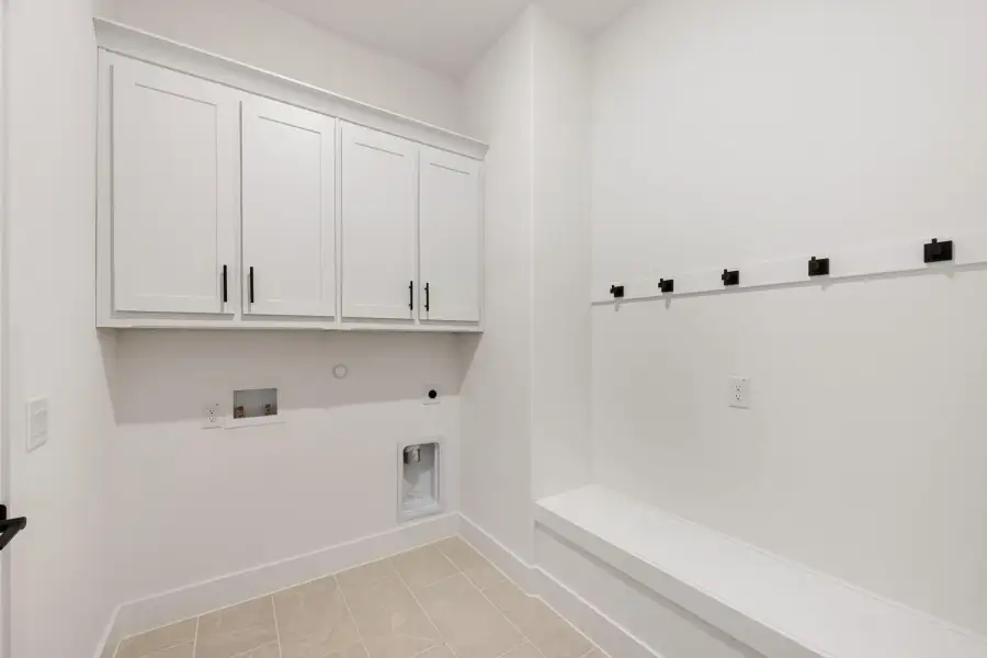 Laundry and mudroom area with white upper cabinets, built-in bench, and black coat hooks on tile floor