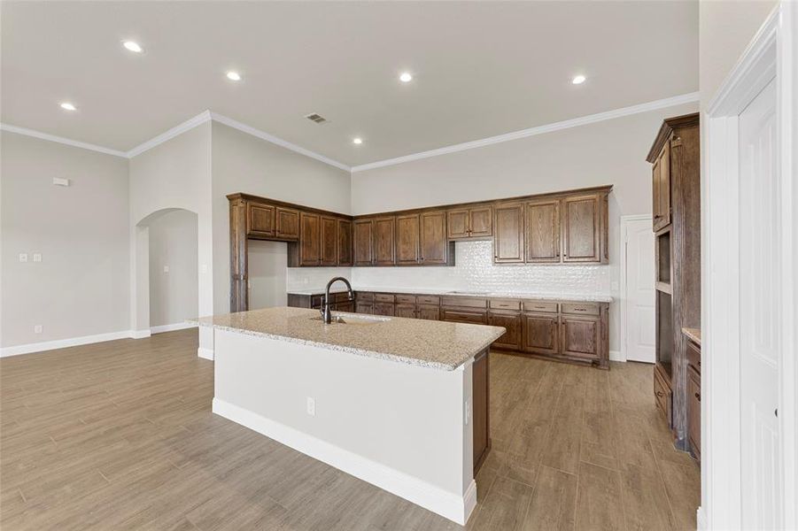 Kitchen with light hardwood / wood-style floors, light stone countertops, sink, and an island with sink