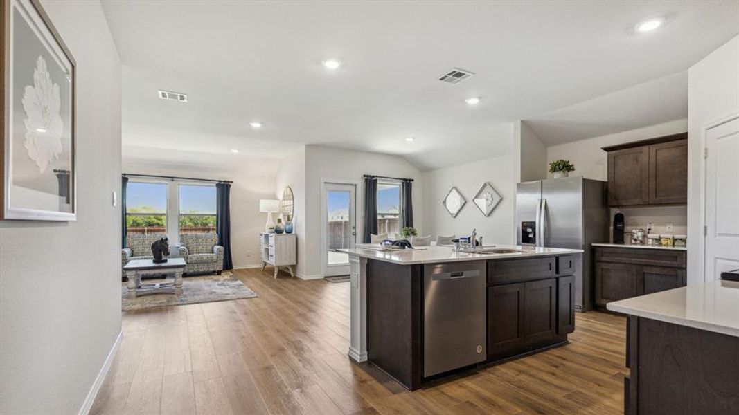 Kitchen with dark wood finish cabinets, stainless steel appliances, dark wood-style floors, a kitchen island with sink, and light stone countertops