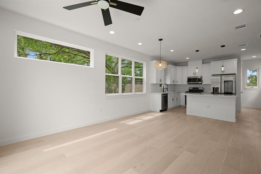 Kitchen featuring stainless steel appliances, open floor plan, white cabinetry, a center island, and light countertops