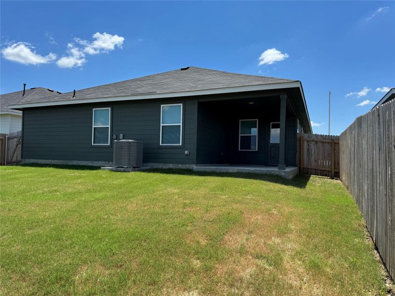 Expansive backyard with a covered patio, dark gray siding, and a wooden privacy fence