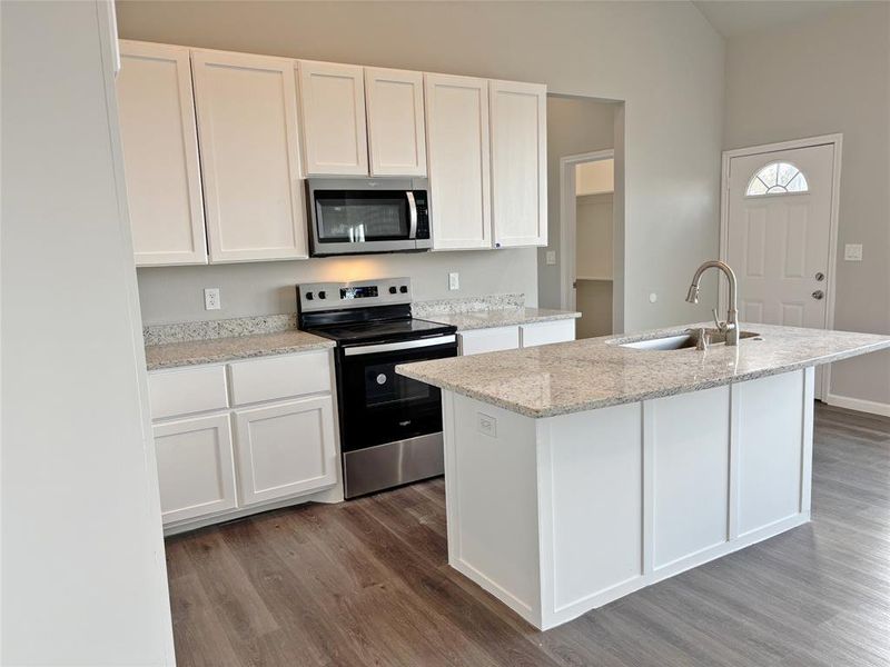 Kitchen with white cabinets, stainless steel appliances, light stone counters, and a center island with sink