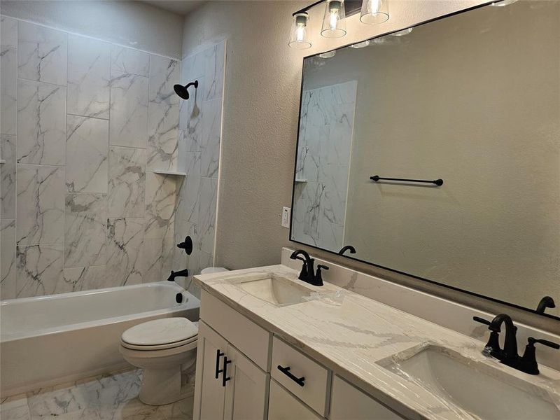 Full bathroom featuring dual vanity, toilet, tiled shower / bath combo, and tile patterned flooring