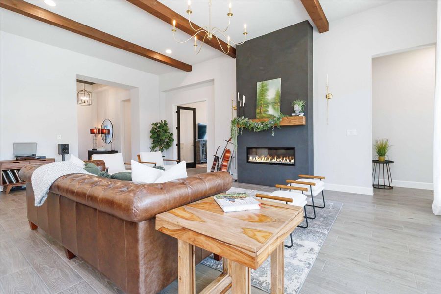 Living room with a chandelier, beamed ceiling, wood tiled floors, and a large fireplace Living room with a chandelier, beamed ceiling, wood tiled floors, and a large fireplace