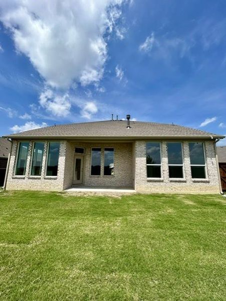 Expansive rear exterior featuring a brick facade, numerous large windows, a covered patio, and a verdant lawn Expansive rear exterior featuring a brick facade, numerous large windows, a covered patio, and a verdant lawn