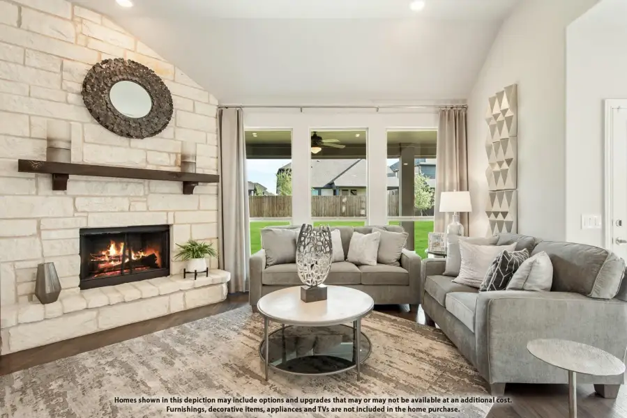 Living room with floor-to-ceiling stone fireplace, gray sofas, vaulted ceiling, and large windows overlooking backyard.