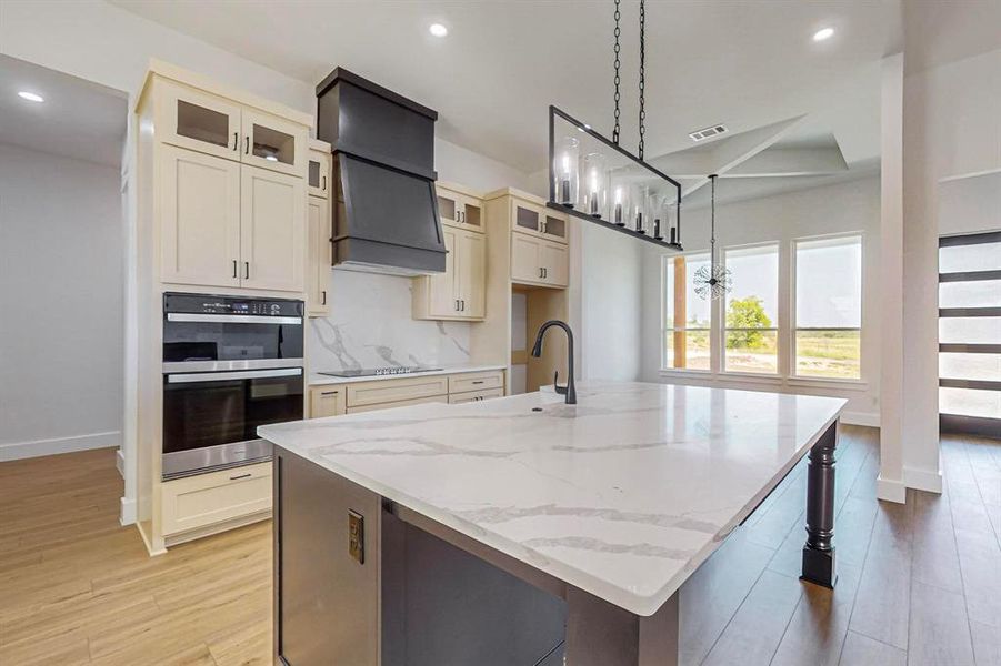 Kitchen featuring light wood-type flooring, stainless steel double oven, tasteful backsplash, and custom exhaust hood