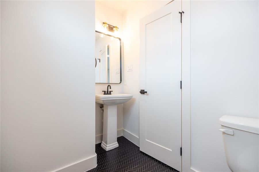 Discreetly tucked to the right of the staircase, out of the main sightline, a conveniently placed half bath is easily accessible to both residents and guests. The dark tile herringbone pattern floors add a touch of sophistication and contrast to the space