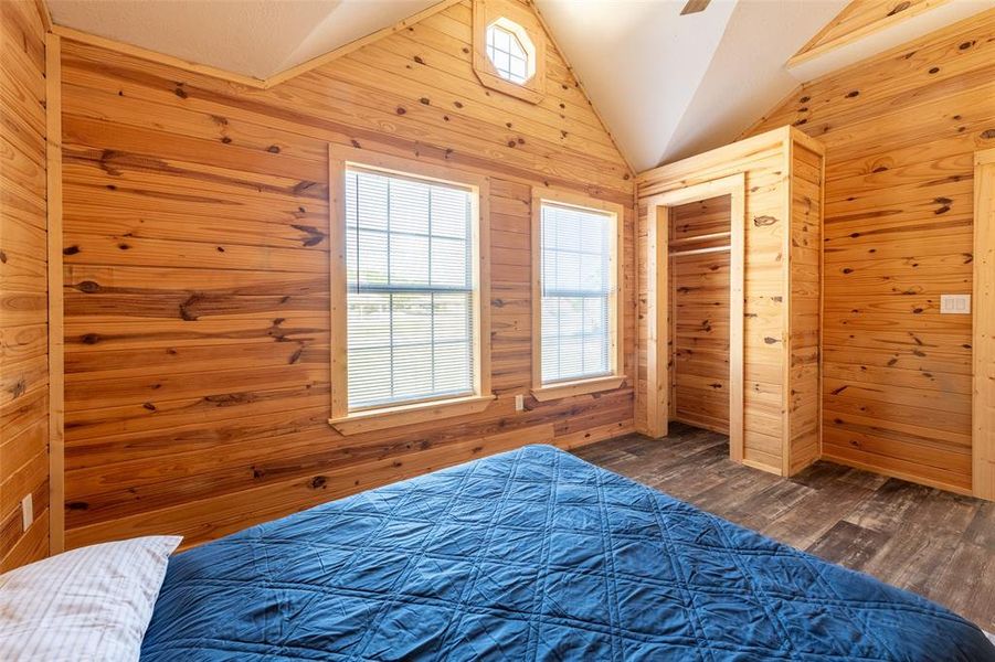 Bedroom featuring extensive wood paneling, a vaulted ceiling, and wood-finish flooring