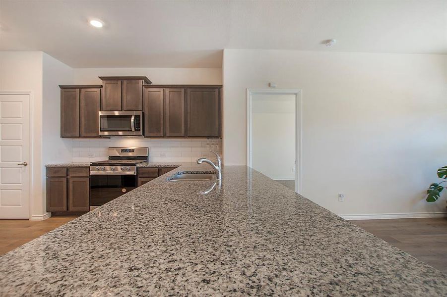 Kitchen featuring dark wood-type flooring, stainless steel appliances, sink, light stone countertops, and tasteful backsplash