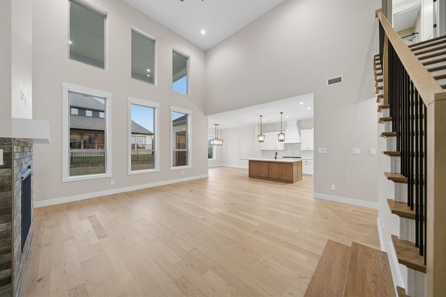 Unfurnished living room with light wood-type flooring, a fireplace, stairs, recessed lighting, and a high ceiling