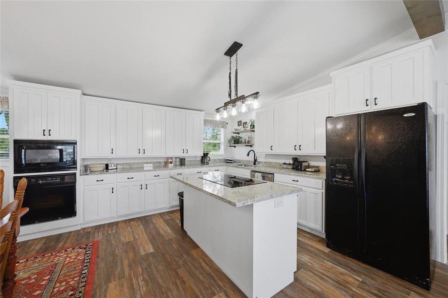 Kitchen featuring white shaker-style cabinetry, granite countertops, wood-finish flooring, a central island with an integrated cooktop, and an integrated wall oven and microwave
