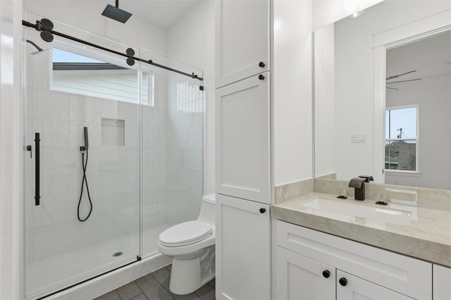 The ensuite bath showcases a sliding glass walk-in shower paired with porcelain countertops and linen cabinetry, creating a polished and comfortable everyday space.