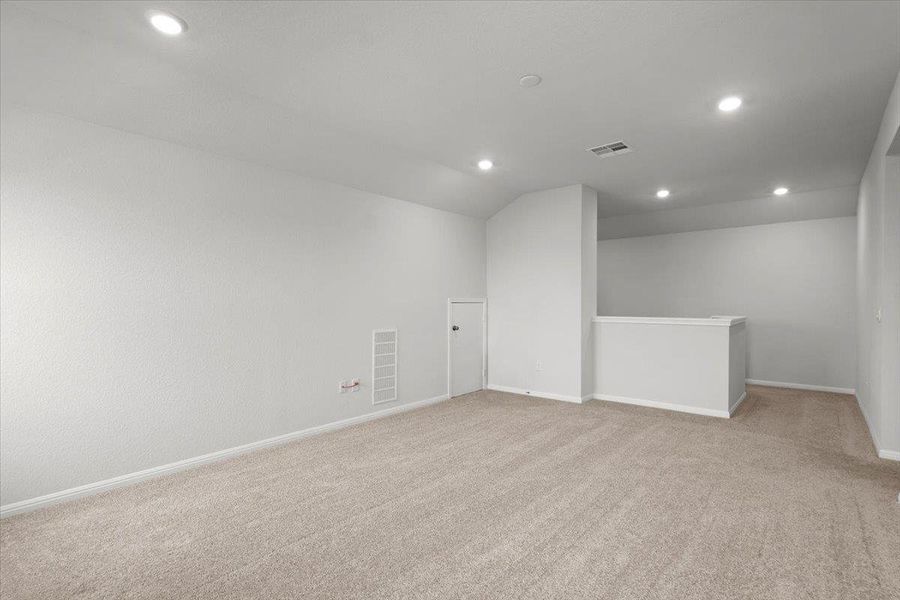 Spacious upper-level room featuring light gray carpeting, neutral wall finishes, recessed lighting, and a white half-wall railing