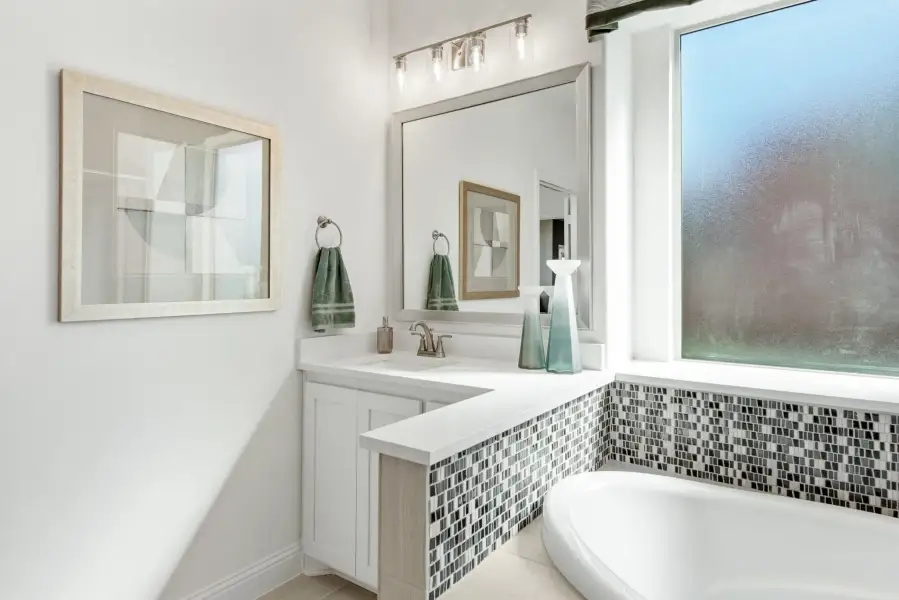Bathroom with white vanity, mosaic tile soaking tub surround, large mirror, and window with natural light