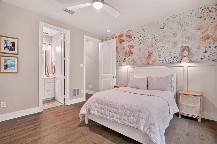 Hardwood-finish flooring extending into a bedroom featuring a decorative floral accent wall with wainscoting and wall-mounted sconces Hardwood-finish flooring extending into a bedroom featuring a decorative floral accent wall with wainscoting and wall-mounted sconces
