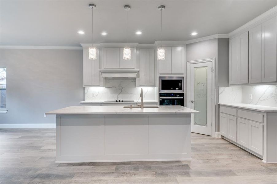 Kitchen with sink, crown molding, decorative light fixtures, an island with sink, and oven